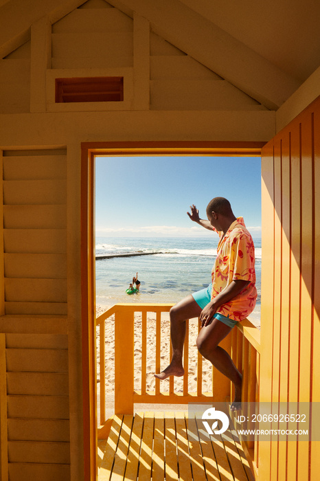 Young father waving at family from beach side cabana in Cape Town