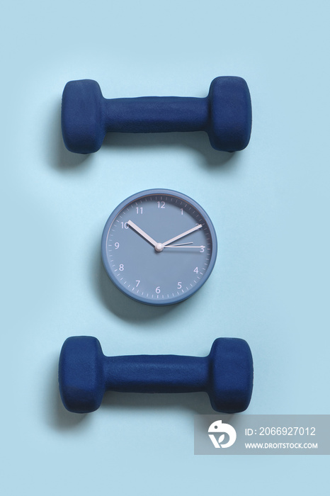 Clock and pair of dumbbells on blue pastel background.