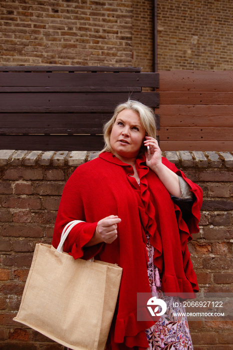 Plus-sized woman having a phone call while holding a reusable grocery bag