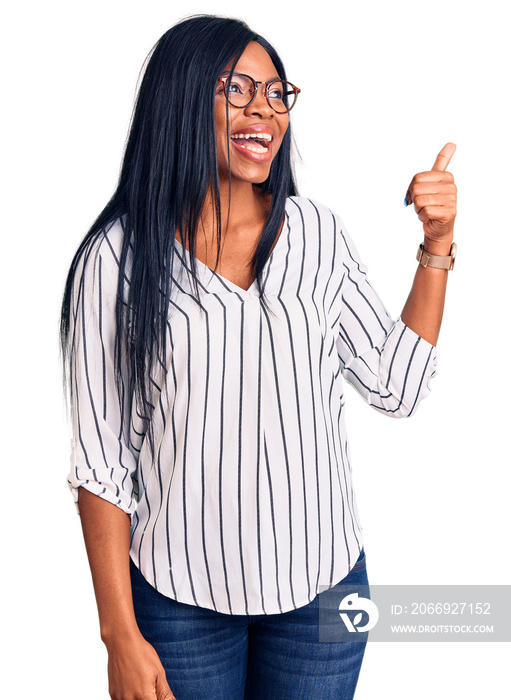 Young african american woman wearing casual clothes and glasses smiling with happy face looking and pointing to the side with thumb up.