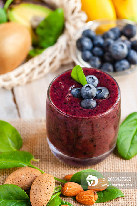 Healthy food and vegan diet concept - fresh juice or smoothie with blueberry, spinach, banana, kiwi, almond milk. Detox beverage with raw ingredients.  Wooden background, close up, macro