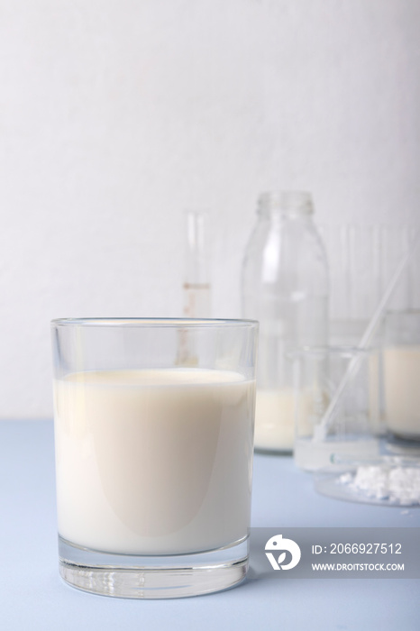 Vertical image.Closeup of glass of milk, lab glassware on the blue surface against white wall