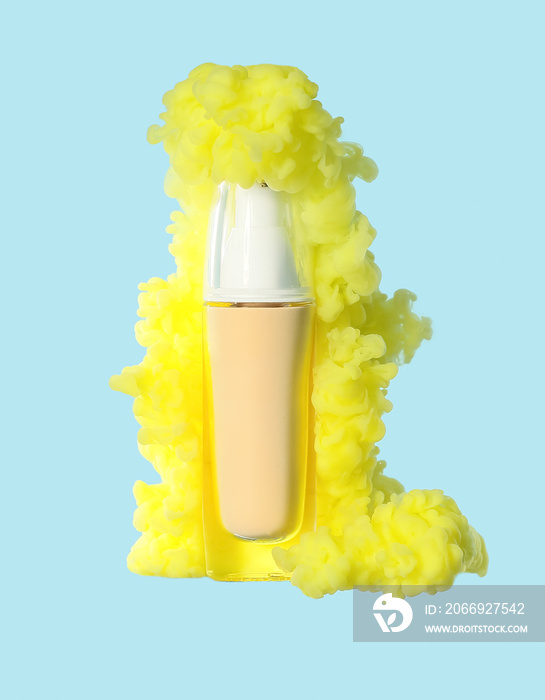 Bottle of makeup foundation in yellow smoke on blue background