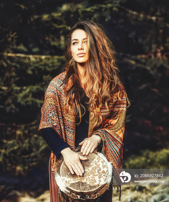 beautiful shamanic girl playing on drum in the nature.