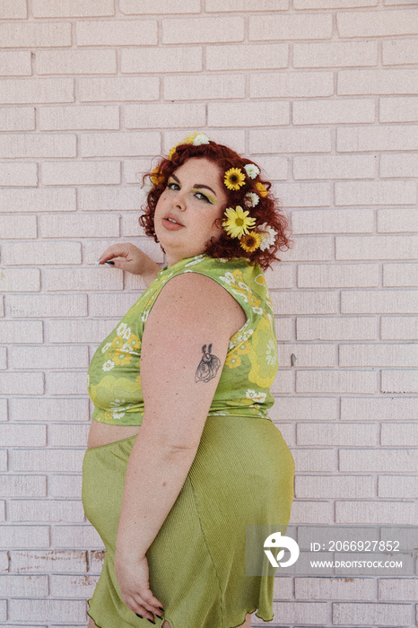 plus size woman standing against pink brick wall looking over shoulder