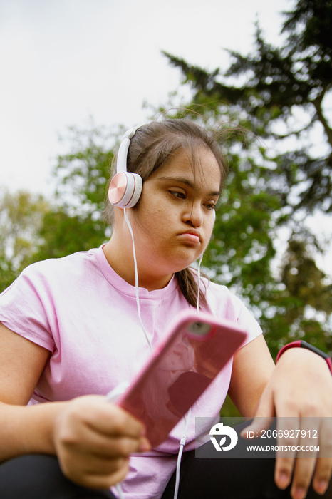 Young curvy girl with Down Syndrome relaxing and listening to music after workout