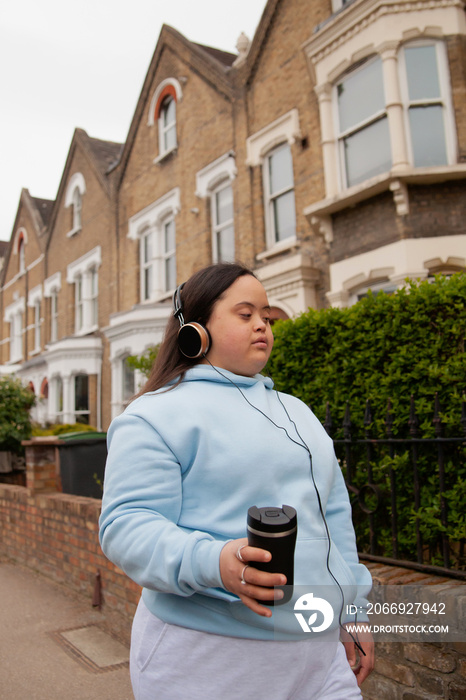 Curvy women with Down Syndrome wearing headphones and holding coffee cup