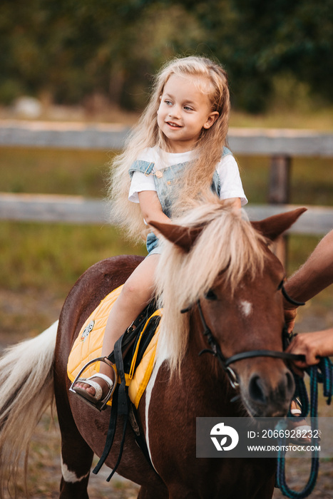 Adorable little girl riding a pony at summer