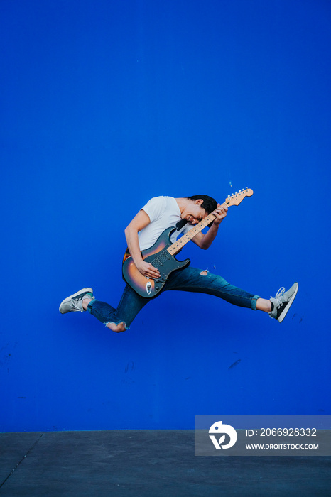 young man jumping with electric guitar on blue background