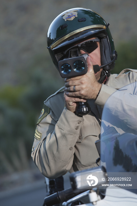 Middle aged policeman monitoring speed through radar while sitting on bike