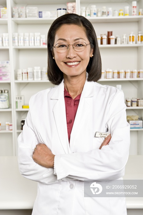 Portrait of a confident smiling female pharmacist standing with hands folded