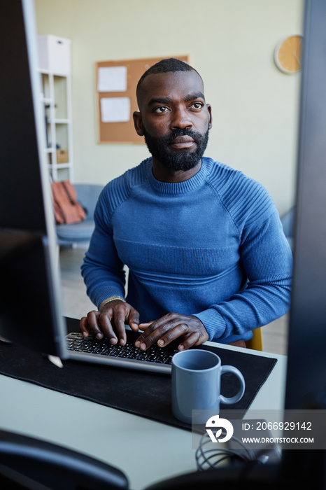 Vertical portrait of focused black man programming software at workplace with multiple computer screens