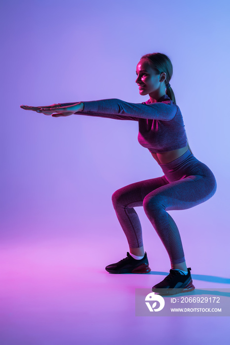 Sport woman doing squatting exercise isolated purple background