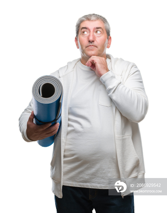 Handsome senior man holding yoga mat over isolated background serious face thinking about question, very confused idea