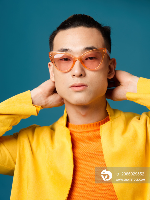 Man in orange glasses blue background asian appearance yellow jacket