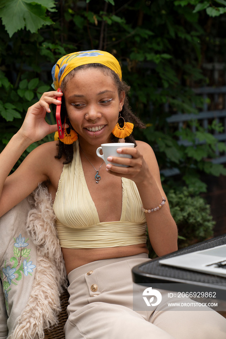 Young woman drinking tea while talking by smart phone in garden