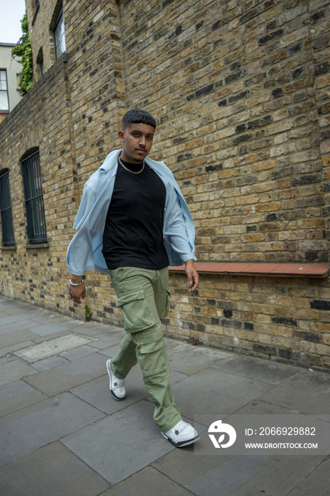 Man wearing unbuttoned shirt and cargo pants walking along brick wall