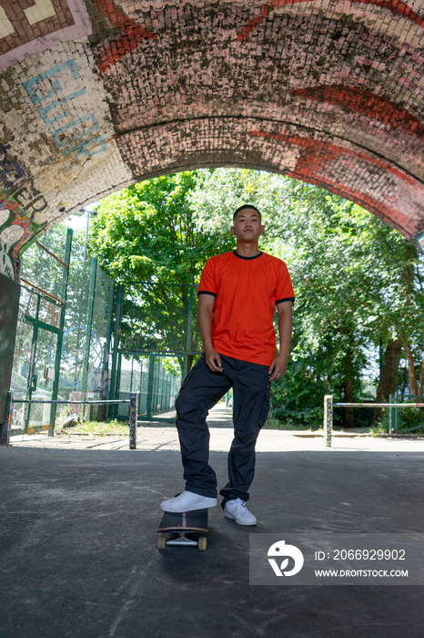 Portrait of young male skateboarder standing under brick arch