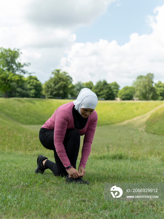 UK,Sutton,Woman in headscarf and sports clothing tying shoe in meadow