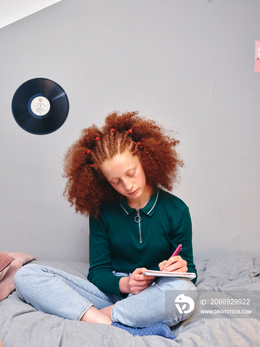 Girl sitting on bed and writing in notepad