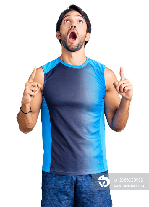 Handsome hispanic man wearing sportswear amazed and surprised looking up and pointing with fingers and raised arms.