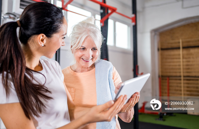 Trainer working with senior woman at the gym using tablet