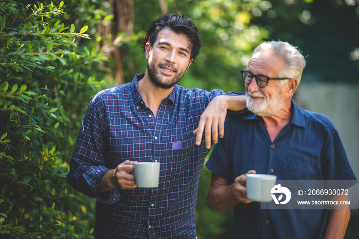 adult son and elderly senior father talking together and holding coffee cup in the garden, happy morning lifestyle of man generation family, love day at home