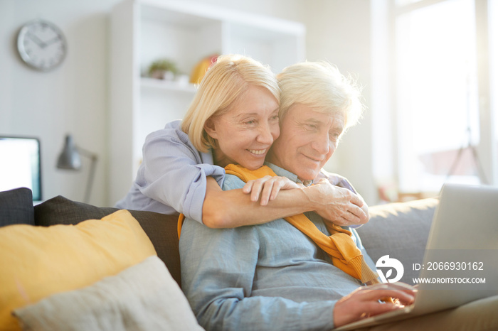 Portrait of happy senior woman embracing husband working with laptop in sunlight, copy space