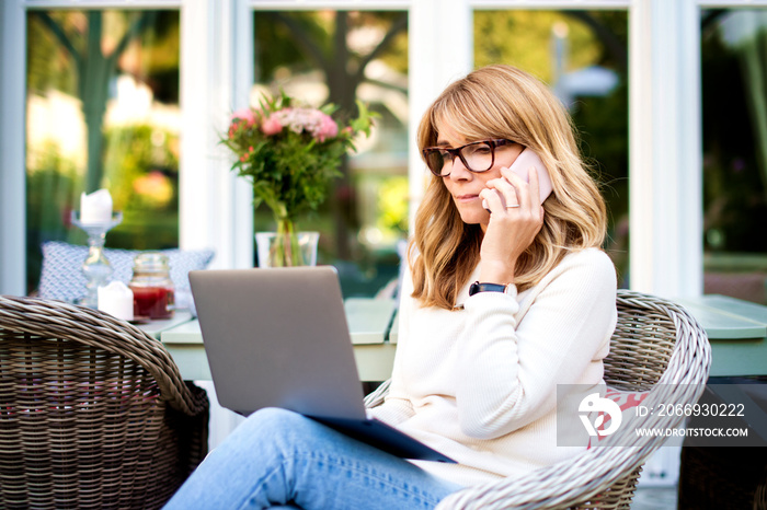 Shot of middle aged woman using laptop and mobile phone while working from home