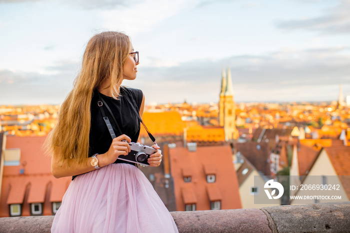 Young woman traveler enjoying beautiful cityscape view sitting with photo camera during the sunset in Nurnberg city in Germany