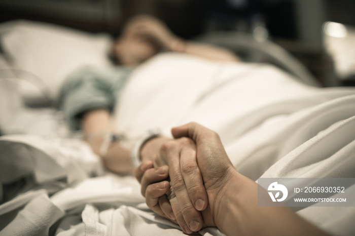 Sick woman in hospital bed with someone holding their hand giving them comfort.