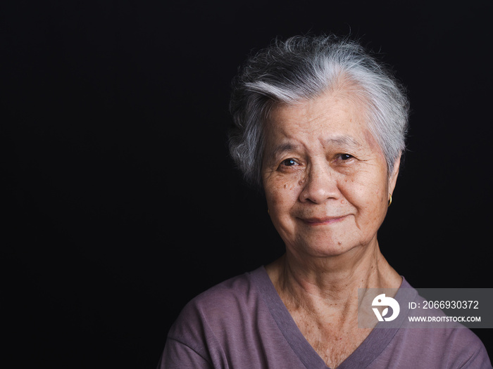 Portrait of a senior woman with short gray hair looking at the camera with a smile with standing on black background in the studio. Space for text. Aged people and health care concept