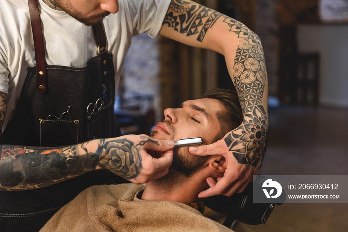 old razor in tattooed hands of stylist