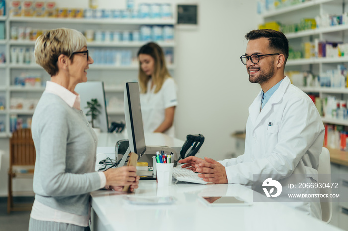 Young male pharmacist giving prescription medications to senior female customer in a pharmacy