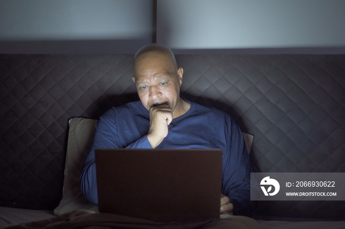 Depressed elderly black man. African American people using a notebook laptop computer on social media internet on bed in bedroom at home. Lifestyle on late night in technology device concept. Insomnia