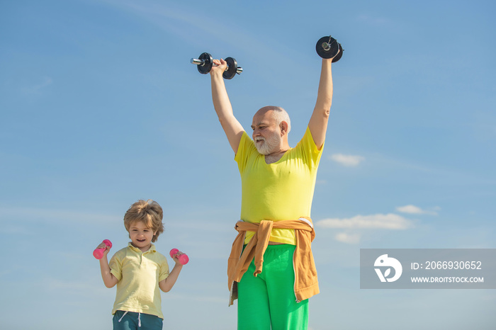 Active healthy life for family. Sports coach and kid building strength with dumbbells. Happy little boy with grandfather is doing exercises with dumbbells.