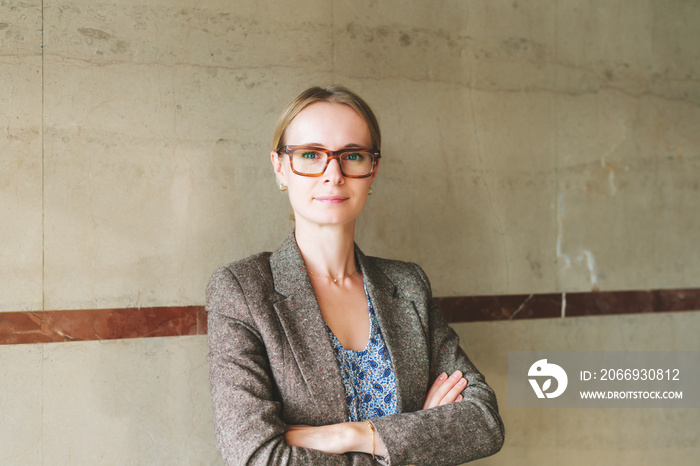 Portrait of yong 35 year old woman wearing brown eyeglasses and jacket, arms crossed