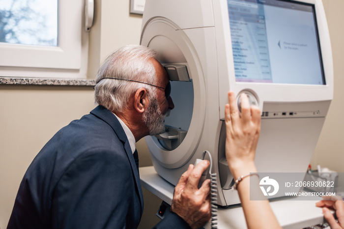 Elegant senior bearded man receiving ophthalmology treatment. Doctor ophthalmologist checking his eyesight with modern equipment.