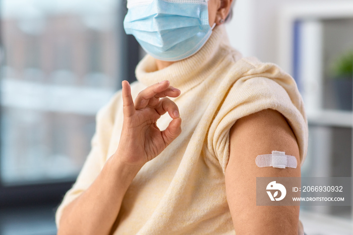 medicine, health and vaccination concept - close up of vaccinated senior woman with medical patch on arm showing ok gesture at hospital