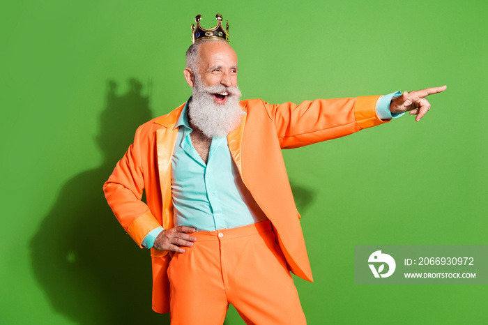 Portrait of retired cheerful cool grey-haired man wearing crown showing copy space isolated over bright green color background