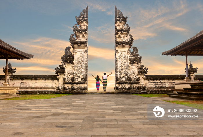 Asian couple standing in the gates of the temple  holding each other’s hand. Sunset in Pura Lempuyang, Bali, Indonesia