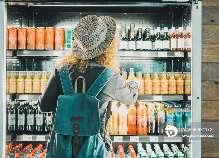 Back view of woman tourist with backpack in front of a window store full of drinks bottles choosing one to buy and drink. Concept of travel solo female people in front of an automatic machine