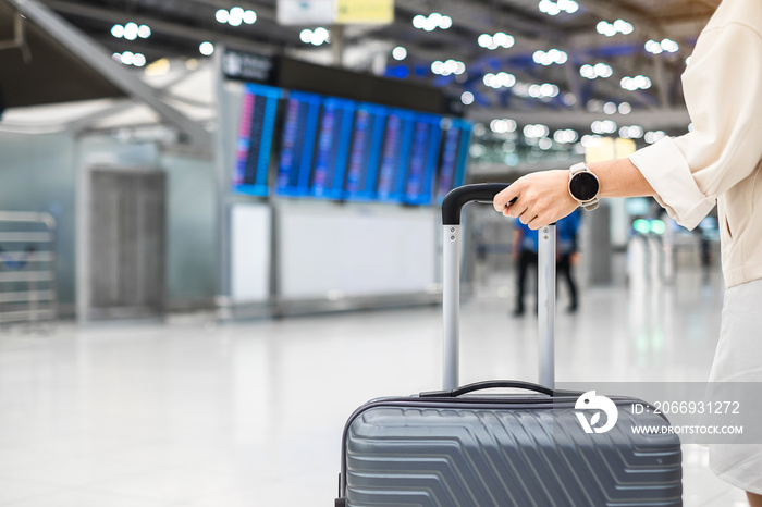 Young woman hand holding luggage handle before checking flight time in airport, Transport, insurance, travel and vacation concepts