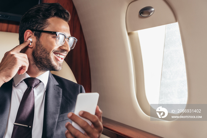 smiling businessman listening music and using smartphone in private plane