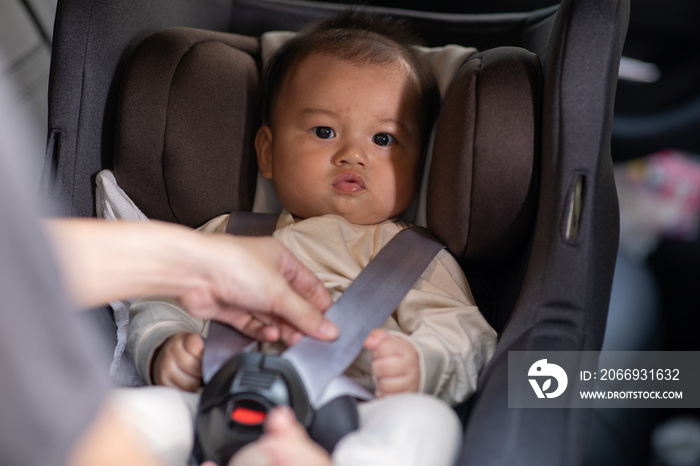 Mother put cute baby to car seat and secure with safety belts. Asian infant baby sit in baby seat and looking around in car.mom buckling her son to car seat.Baby safety on car concept