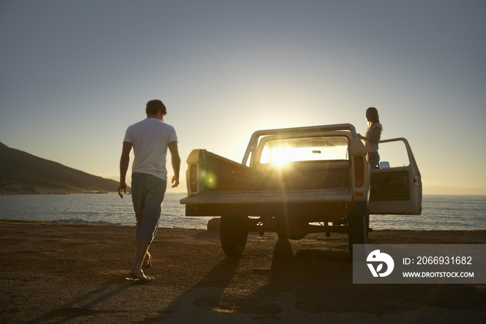 Full length of young couple by pick-up truck parked on beach