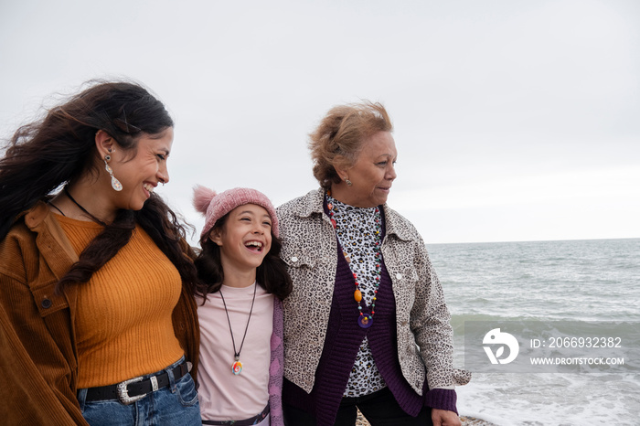 Grandmother, mother and daughter walking on beach on cloudy day