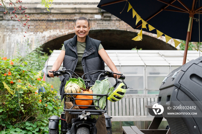 Smiling woman riding cargo electric trike loaded with homegrown vegetables