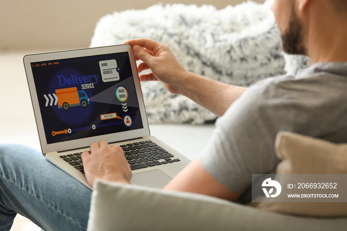 Young man using laptop with open page of delivery service application at home