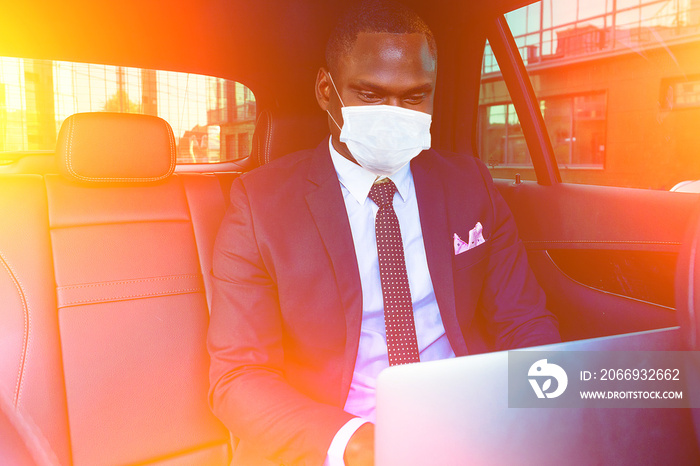 Handsome successful rich african american business men entrepreneur in a stylish black suit and tie sitting in a luxury car and works with laptop